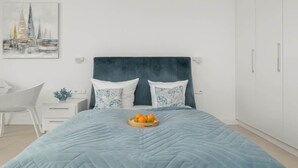 A bedroom with a bed, a bedside table, a chair, and a wall-mounted artwork.