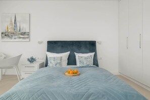 A bedroom with a bed, a bedside table, a chair, and a wall-mounted artwork.