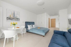 Ein modernes Schlafzimmer mit einem Bett, einem blauen Sofa, einem Esstisch mit Stühlen und einem Bild an der Wand.