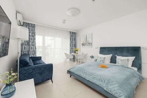 A modern bedroom with a large bed, a sofa, a dining table, and a chair.