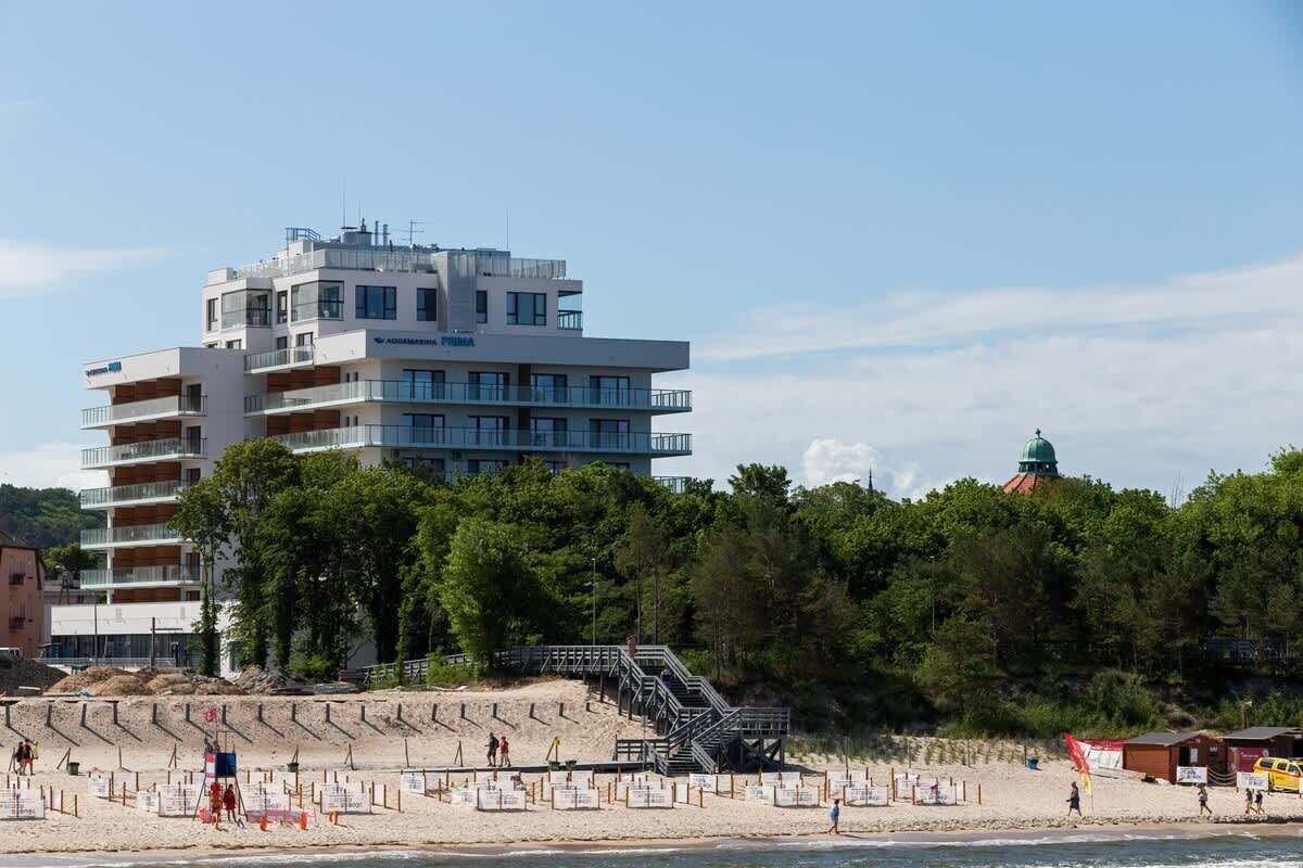 Un hôtel moderne à plusieurs étages, doté de balcons et d’un espace de plage accessible par un escalier.