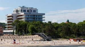 A modern hotel with multiple floors, balconies, and a beach area with a staircase leading to the beach.