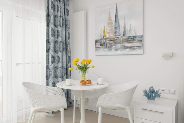 A modern room with a round table, two white chairs, a vase with yellow flowers, and a painting of sailboats on the wall.