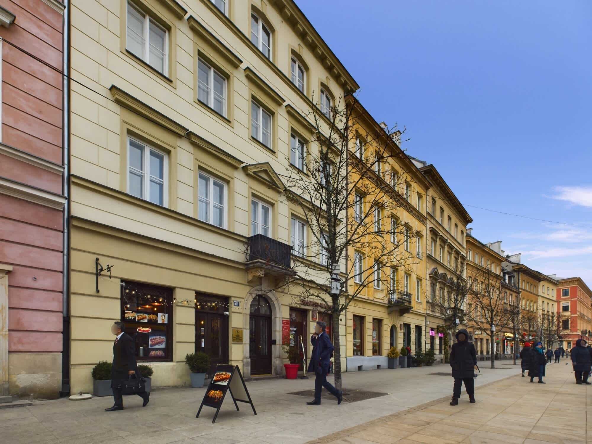 A street with buildings, a sidewalk, and a few pedestrians.