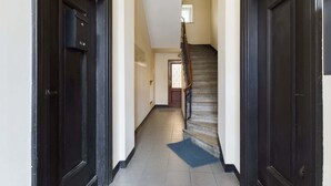 A hallway with dark wooden doors, a tiled floor, and a staircase with a wooden handrail. - Stylish Studio | Krakowskie Przedmieście, in the heart of Warsaw (Warszawa)