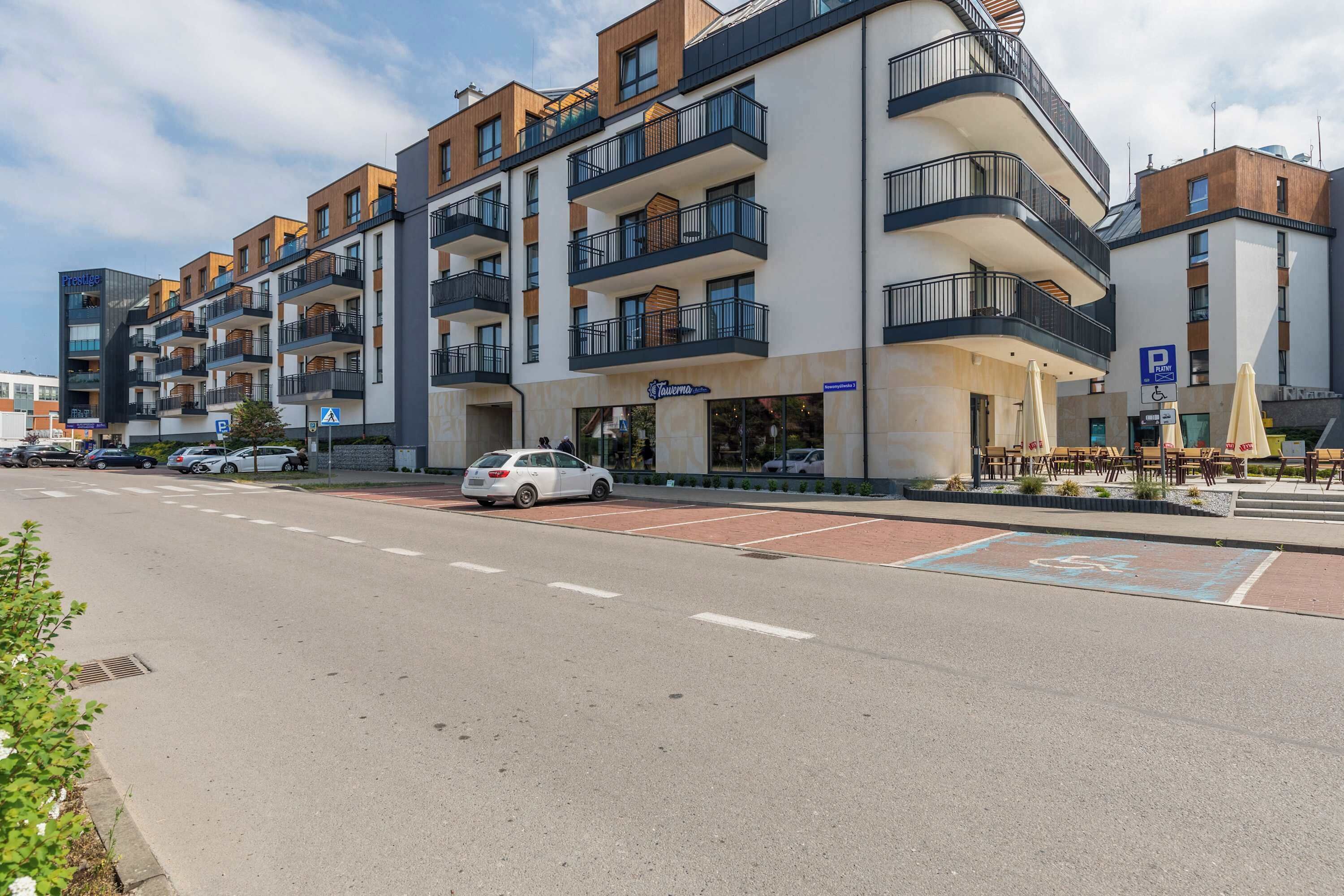 Um hotel moderno de vários andares com varandas, área de estacionamento e mobiliário para áreas externas.
