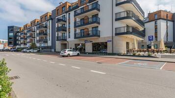 Um hotel moderno de vários andares com varandas, área de estacionamento e mobiliário para áreas externas.