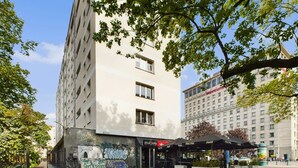 Ein modernes Gebäude mit flacher Fassade, einem gut sichtbaren Eingang und einem Außenbereich mit Sitzgelegenheiten und Sonnenschirmen.