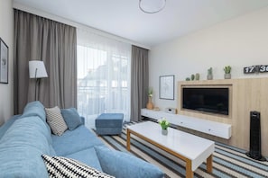 Uma sala de estar moderna com sofá, repouso para os pés, mesa de centro, televisão e uma pequena planta.