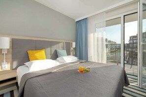 A hotel room with a bed, a nightstand, a lamp, a fruit basket, and a view of the city through a glass door. - Spacious Apartment for 8 Persons | 3 Bedrooms | Parking. (Międzyzdroje)