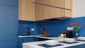 A modern kitchen with blue walls, wooden cabinets, and a white countertop. - Stylish Apartment in the Center | Workplace (Warszawa)
