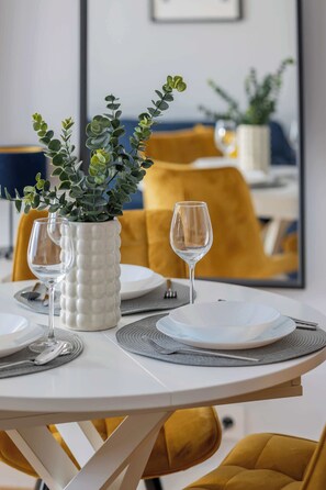 A dining table set with white plates, silverware, and a white vase with green foliage. - Elegant Apartment in Bemowo | Parking and Balcony (Warszawa)