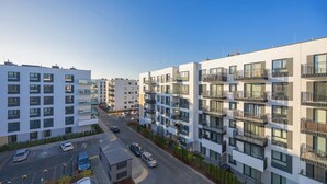 Ein modernes Mehrfamilienhaus mit mehreren Balkonen und einem Parkplatz davor.