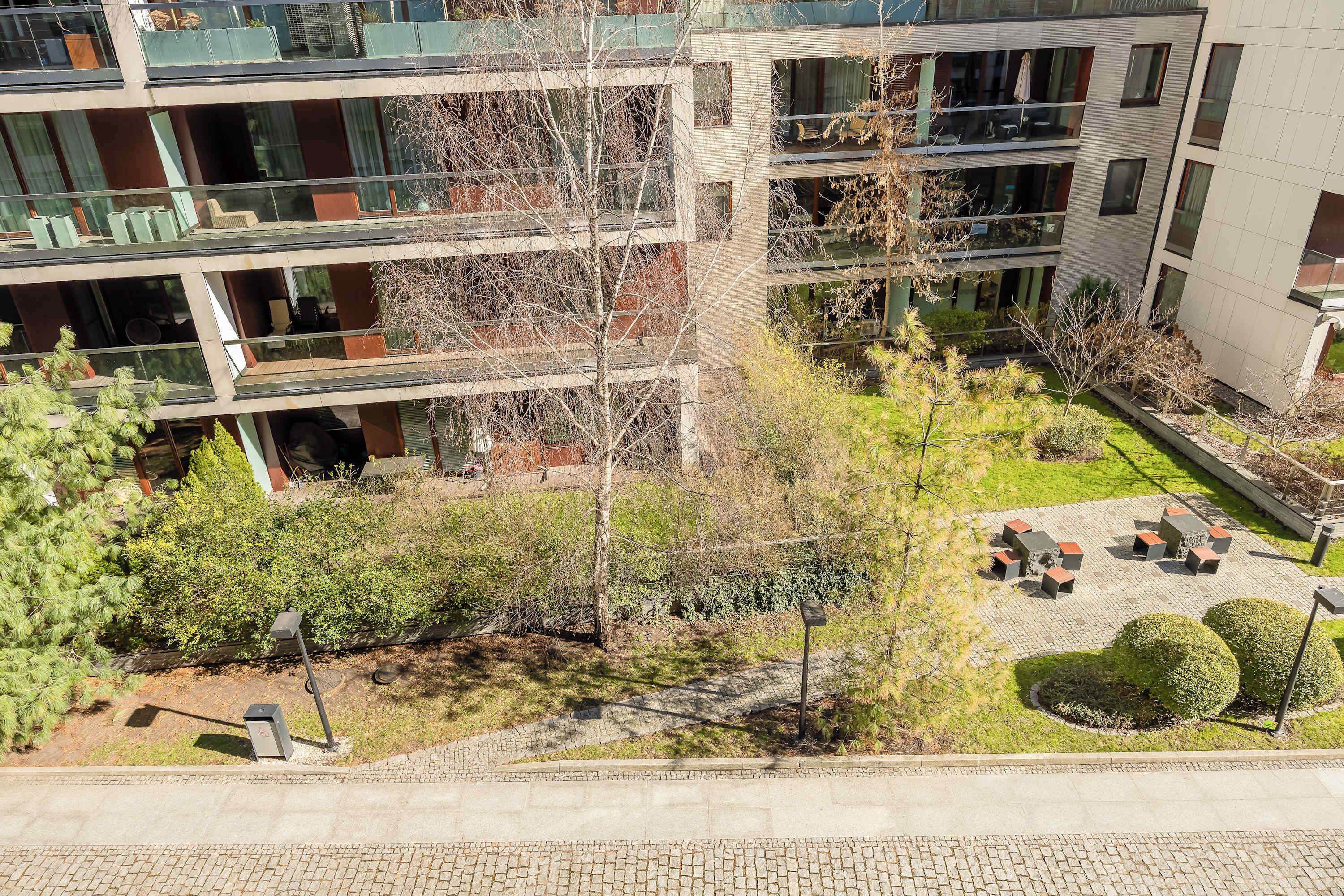 Un edificio de varios pisos con balcones, un patio con asientos y una pequeña zona de jardín.