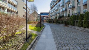 Une rue urbaine moderne bordée d’immeubles résidentiels à plusieurs étages, avec un trottoir pavé et des espaces aménagés.