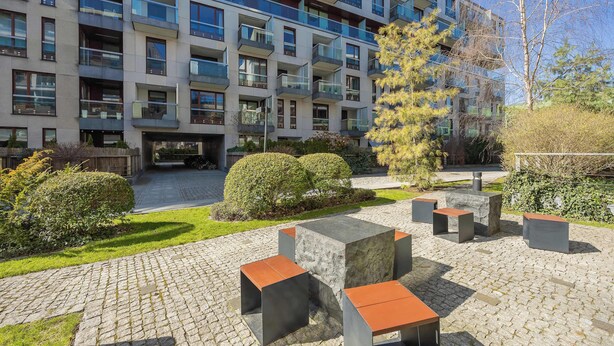 Un immeuble d’appartements moderne doté de nombreux balcons, d’une cour avec des bancs en pierre et d’un espace vert bien entretenu.
