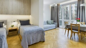 Un dormitorio moderno con dos camas, un sofá, una mesa de comedor con sillas y ventanas amplias con vistas a edificios.