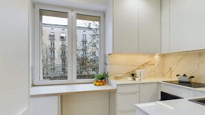 Una cocina moderna con armarios blancos, un salpicadero de mármol y una ventana con vistas a una zona residencial.