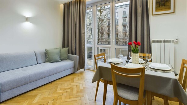 Un área de comedor con una mesa dispuesta para dos personas, un sofá y una ventana con cortinas.