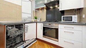 Una cocina compacta con armarios blancos, horno empotrado, microondas y lavavajillas.