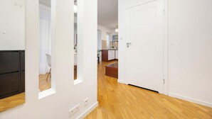 Un apartamento moderno con piso de madera, paredes blancas y una cocina visible a través de una puerta abierta.
