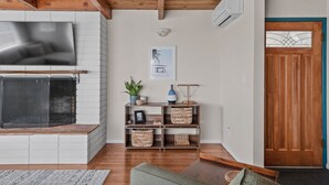 A living room with a fireplace, wooden beams, a TV, a door, and a shelf with baskets.