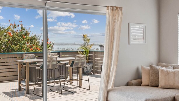 A balcony with a table and chairs, a sofa, and a view of the sea.
