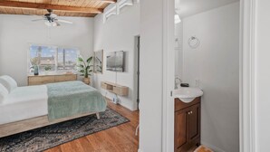 A bedroom with a bed, a ceiling fan, a window with blinds, a bedside table with a plant, and a nightstand.