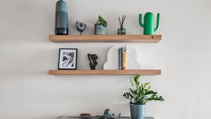 A wooden cabinet with a plant on top, wooden shelves with various items, and a white wall.
