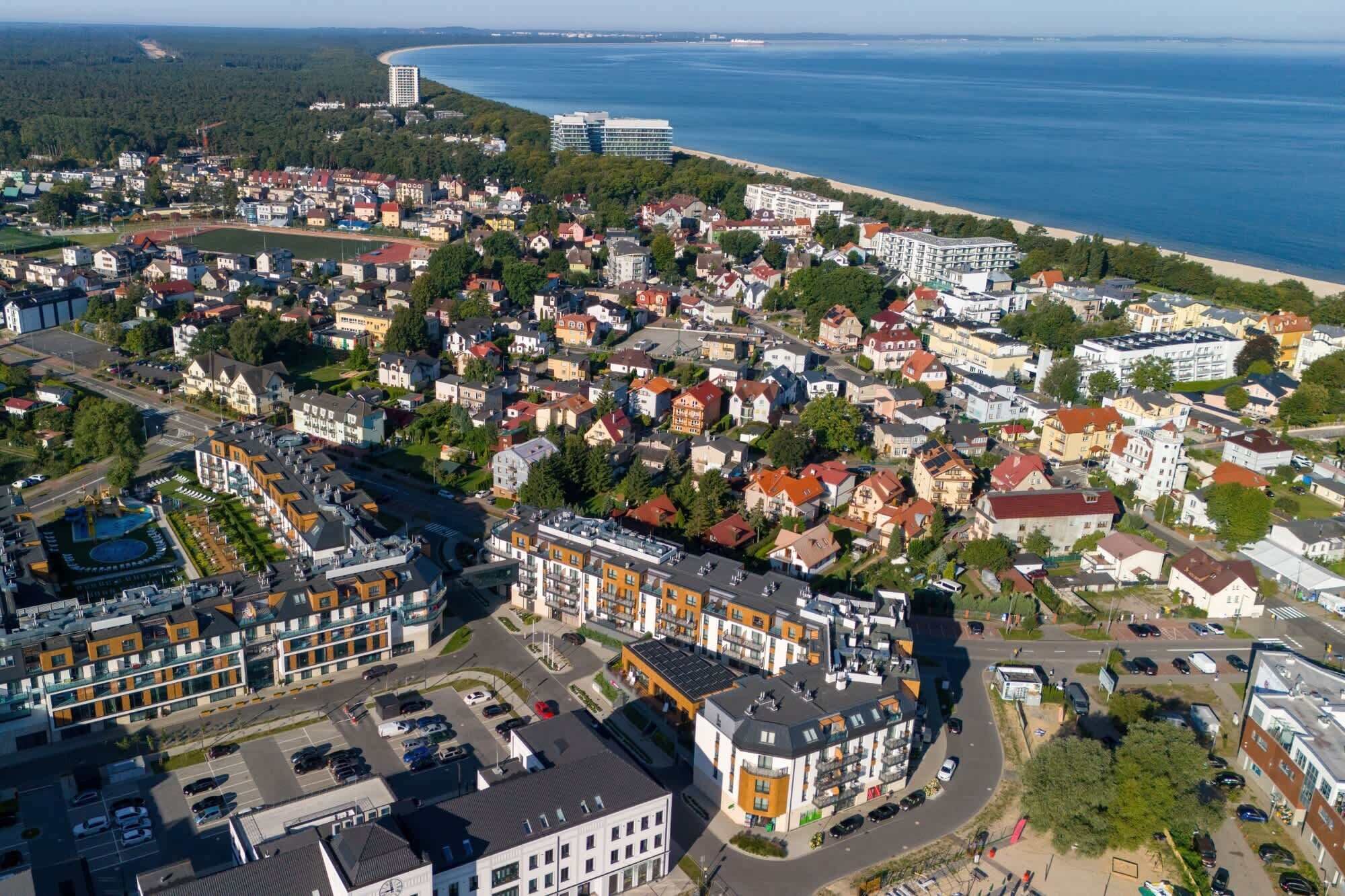 Vista aèria d'una població costanera amb edificis residencials i un hotel destacat de disseny modern i zona de pàrquing.