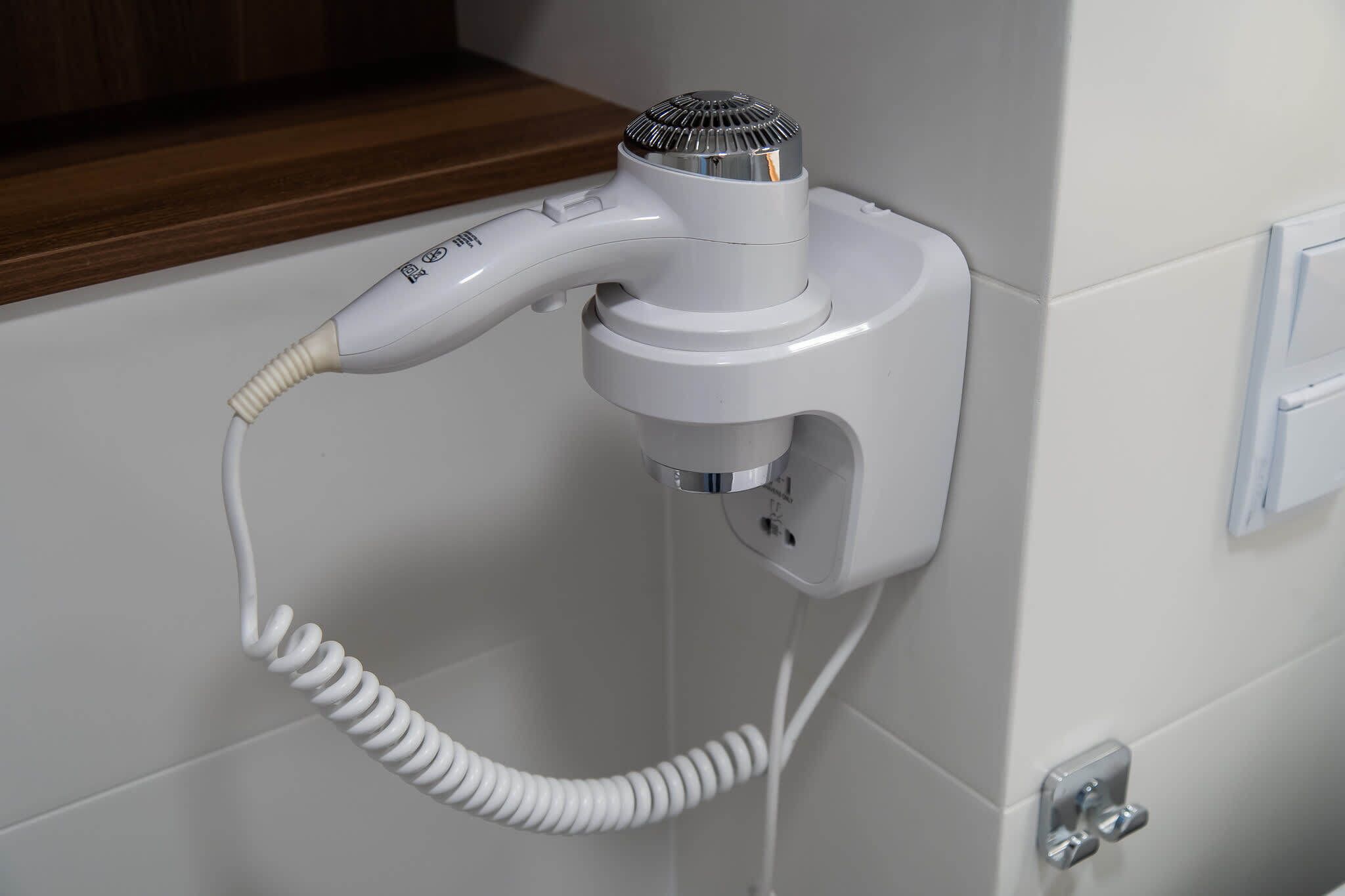 A white hairdryer mounted on a wall with a coiled cord.