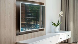 A modern living room with a flat-screen TV mounted on a wooden wall, a white console table with drawers, and a potted orchid.
