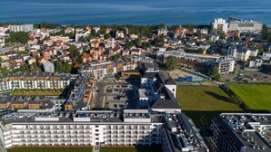 A modern hotel complex with multiple buildings, a parking area, and a view of the sea.