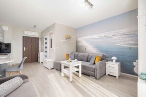 A modern living room with a grey sofa, a white coffee table, and a painting of a beach scene on the wall. - Bright Studio in Miedzyzdroje | Parking | 10 min to the Beach (Międzyzdroje)