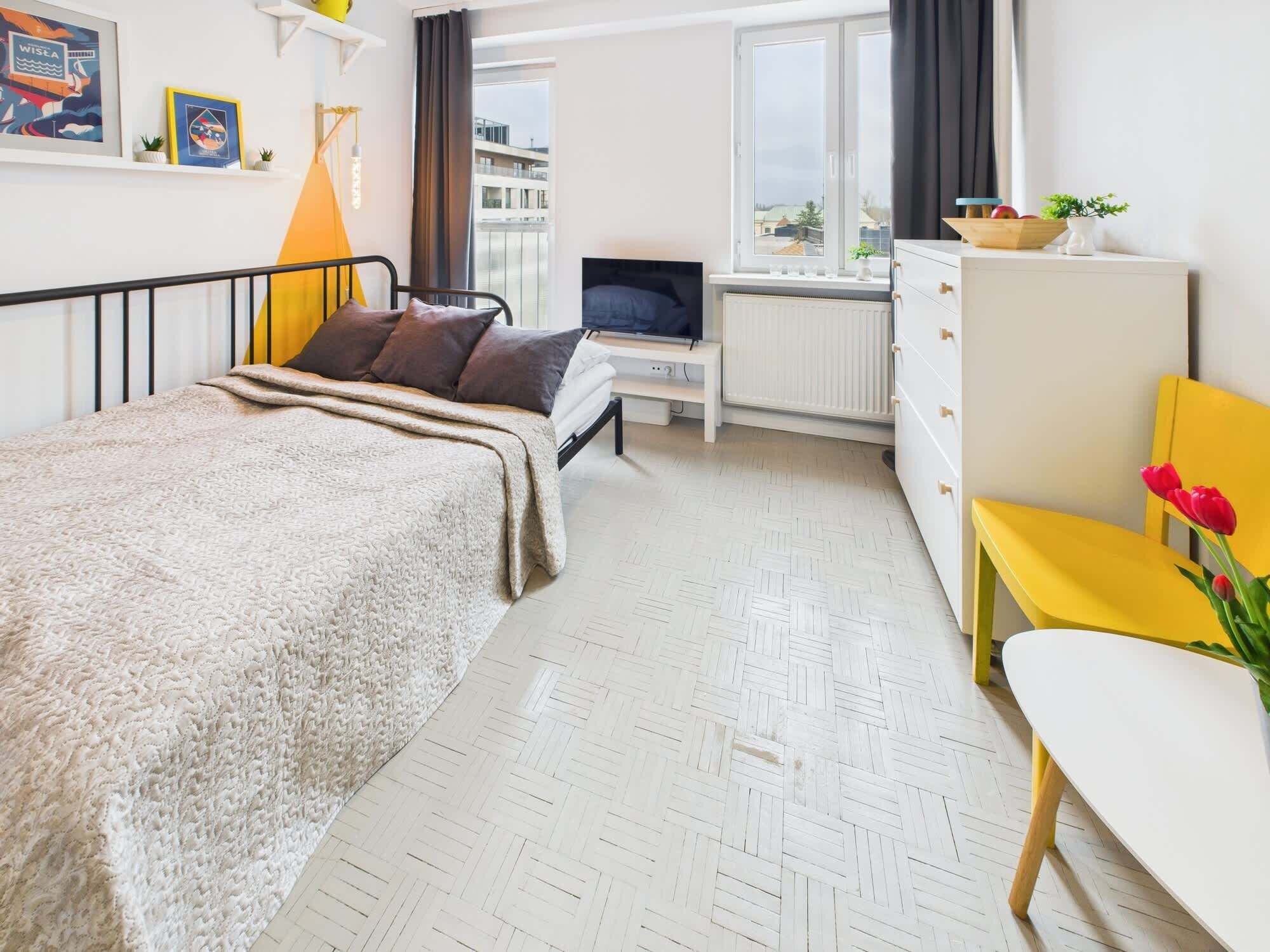 Hotelkamer met een bed, een bureau met een computer, een radiator, een raam met gordijnen en uitzicht op gebouwen.