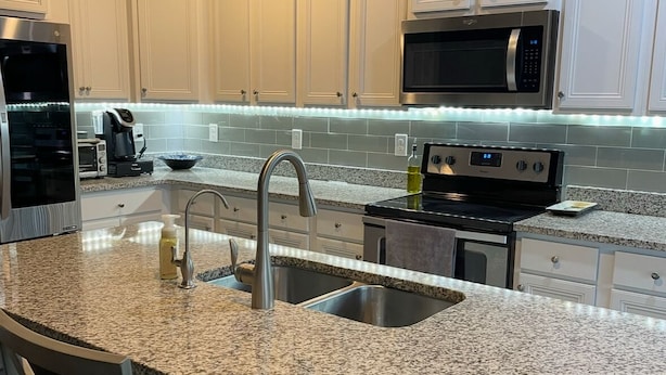 A modern kitchen with white cabinetry, granite countertops, stainless steel appliances, and a built-in island with bar stools. - 3-bedroom house in beautiful Santa Rosa Beach!4,500/month. 3-6 month rental only (Santa Rosa Beach)