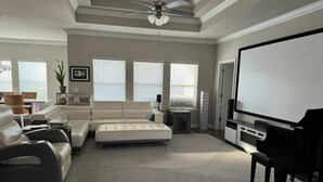 A spacious living room with a sectional sofa, a piano, and a large screen. - 3-bedroom house in beautiful Santa Rosa Beach!4,500/month. 3-6 month rental only (Santa Rosa Beach)