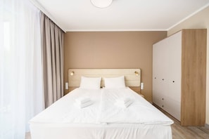 A modern hotel room with a large bed, a wooden wardrobe, and a neutral color scheme.