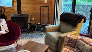 Een gezellige woonkamer met een houtkachel, een comfortabele fauteuil, een ruitjesbank en een houten salontafel.