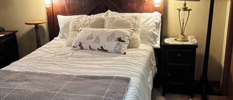 A neatly arranged bedroom with a large bed, a bedside table with a lamp, and a wall-mounted artwork.