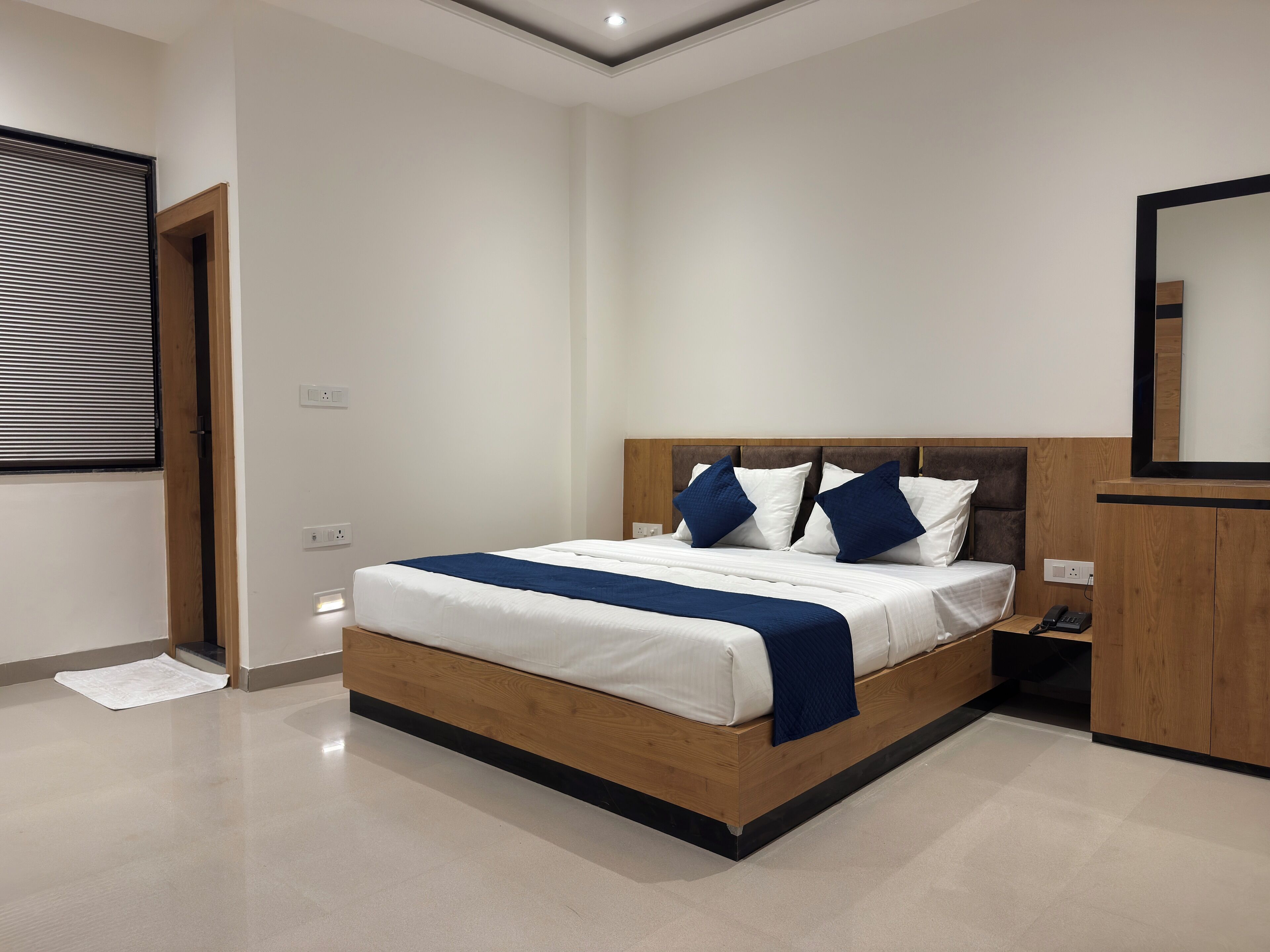 A modern hotel room with a large bed, wooden headboard, and a bedside table with a phone.
