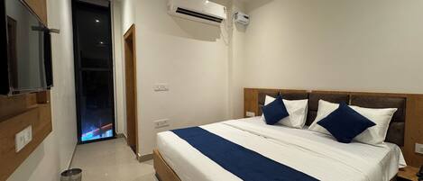Une chambre moderne avec un grand lit, une tête de lit en bois et un téléviseur fixé au mur.