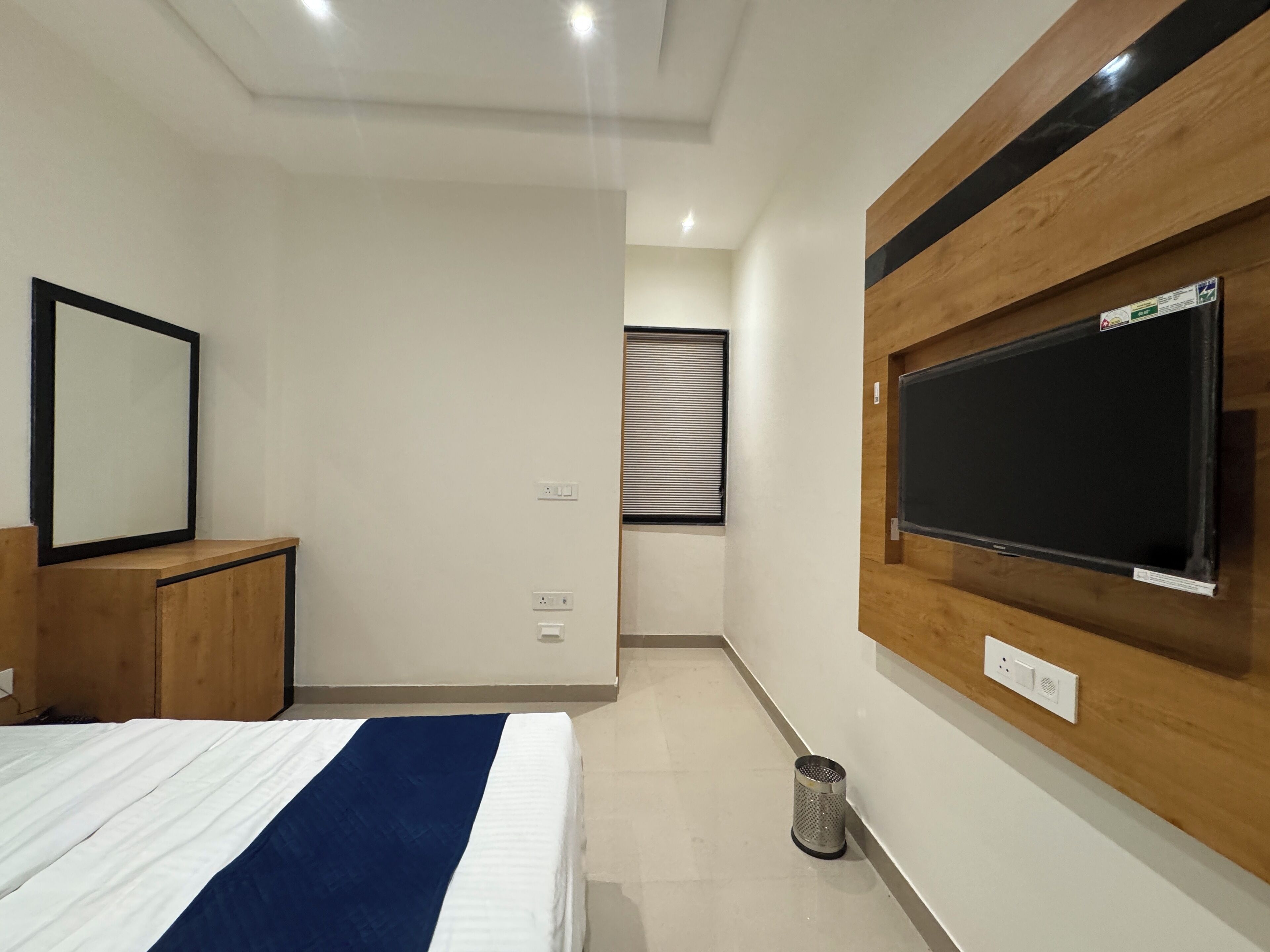 Ein modernes Hotelzimmer mit einem Bett, einem an der Wand befestigten Fernseher, einem Holzschrank und einem Papierkorb.