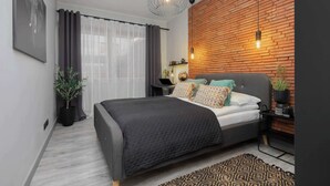 A modern bedroom with a bed, a wooden accent wall, a pendant light, and a potted plant.