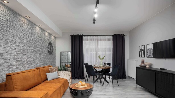 A modern living room with a stone wall, a sofa, a dining table with chairs, and a black cabinet.