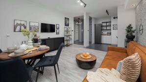 A modern living room with a dining area, featuring a sofa, a coffee table, and a dining table set for four.