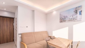 Una sala de estar moderna con un sofá color beige, una mesa de comedor de madera y una pared blanca con un cuadro enmarcado.