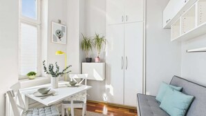 A modern, well-lit room with a dining table, chairs, a grey sofa, and a white cabinet. - Cozy Studio in the Center | Balcony and Proximity to Bathrooms (Warszawa)