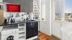 A compact kitchen with a washing machine, a red appliance, and a staircase leading to an upper level. - Cozy Studio in the Center | Balcony and Proximity to Bathrooms (Warszawa)
