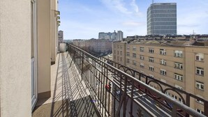 A balcony with a metal railing overlooking a cityscape, featuring several buildings including a tall, modern structure. - Cozy Studio in the Center | Balcony and Proximity to Bathrooms (Warszawa)